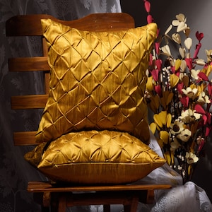 May include: Two gold-colored decorative throw pillows with a quilted diamond pattern. The pillows are sitting on a wooden chair.
