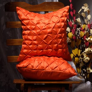 May include: Two orange decorative throw pillows with a quilted design. The pillows are sitting on a wooden chair.