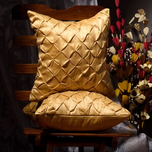 May include: Two gold-colored pillow covers with a quilted diamond pattern. The pillow covers are on a wooden chair.