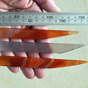 May include: Three agate tools, two are orange with white stripes and one is a light grey. The tools are approximately 5 inches long and are laid out on a ruler.