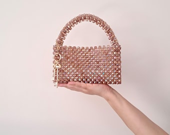 May include: A small, rectangular handbag made of iridescent pink beads with a gold chain handle and a key charm.