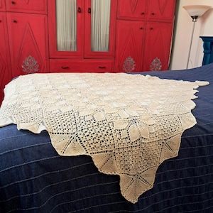 May include: A cream-colored crocheted throw blanket with a delicate floral pattern, draped over a blue bed.