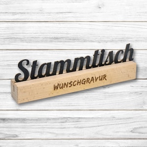 Könnte beinhalten: Ein Holzschild mit dem Wort "Stammtisch" in schwarzen Buchstaben. Das Schild steht auf einem Holzsockel mit den Worten "Wunschgravur" in das Holz graviert.