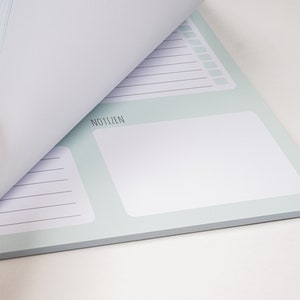 May include: A light blue notepad with a white page turned over. The notepad has a section labeled "Notizen" and lined pages.
