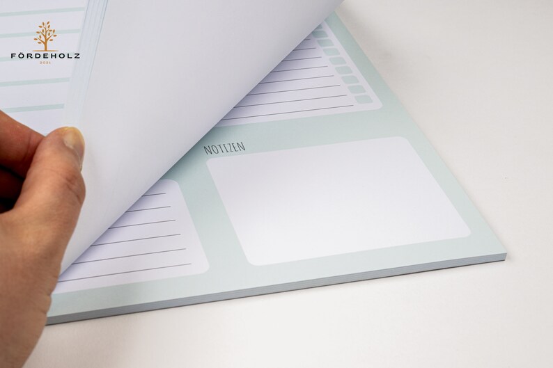 May include: A light blue notepad with a white page turned over. The notepad has a section labeled "Notizen" and lined pages.