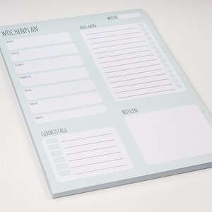 May include: A light blue weekly planner notepad with sections for "Wochenplan" (weekly plan), "Aufgaben" (tasks), "Woche" (week), "Geburtstage" (birthdays), "Notizen" (notes).