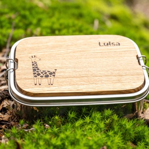 Könnte beinhalten: Eine Edelstahl-Lunchbox mit einem Holzdeckel. Der Deckel hat eine Giraffen-Illustration und den Namen "Luisa" eingraviert.