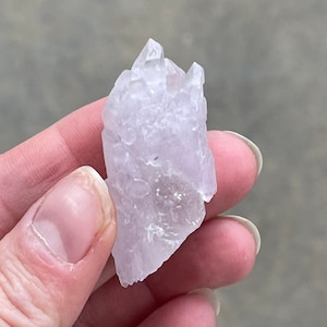 May include: A pale purple crystal cluster with a pointed top and a rough, textured surface.
