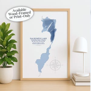 May include: A framed print of Dalrymple Lake in Ontario, Canada, with a light blue topographic map design. The print includes the lake's name, coordinates, maximum depth (11 m / 35 ft), and shoreline length (48 km / 30 mi). The frame is light wood.