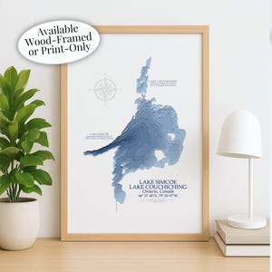 May include: A framed print of Lake Simcoe and Lake Couchiching in Ontario, Canada, with a detailed blue topographical map. The print is in a light wood frame and includes a compass rose graphic. Text on the print reads "Available Wood-Framed or Print-Only."