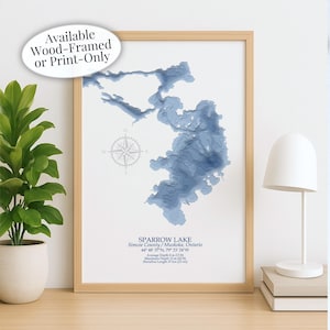 May include: A framed print of Sparrow Lake in Simcoe County, Ontario, with a 3D topographic map in shades of blue. The print includes a compass rose and text indicating the lake's coordinates, average depth of 13 ft, and shoreline length of 23 mi. Text reads: Available Wood-Framed or Print-Only.