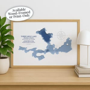 May include: A framed map of Three Mile Lake, Muskoka, Ontario, with a 3D topographic design in blue hues. The map displays coordinates, average and maximum depths, and shoreline perimeter. The frame is light brown. Text reads "Available Wood-Framed or Print-Only".