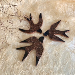 May include: Three ceramic swallow birds with a black and brown floral pattern. The birds are arranged in a circle with their wings spread out.
