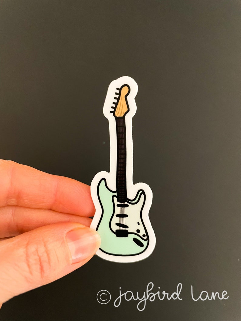 May include: A sticker of a light blue electric guitar with a white pickguard and a brown neck. The sticker is on a dark gray background.