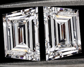 May include: Two clear princess-cut diamonds held by silver tweezers against a black background.