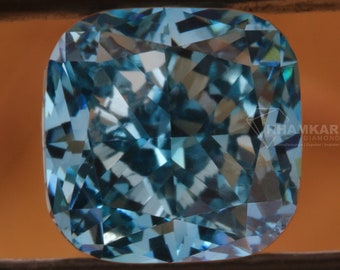 May include: A cushion-cut, light blue gemstone held by black tweezers. The gemstone has many facets, reflecting light. The background is a blurred, warm brown color. The gemstone is a square shape with rounded corners.