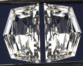 May include: Two clear octagon-shaped gemstones held by a pair of tweezers against a dark blue background.