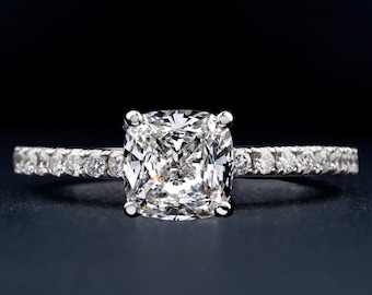 May include: A silver engagement ring with a large, square-shaped diamond in the center. The band is set with smaller diamonds.