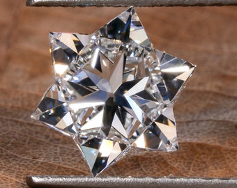Può includere: Un diamante trasparente, sfaccettato, a forma di stella, tenuto da pinzette argentate su uno sfondo marrone testurizzato.