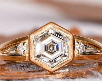 May include: A gold ring with a hexagonal shaped diamond set in a gold bezel. The diamond has a faceted design and is surrounded by smaller diamonds on the band.