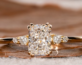 May include: A gold engagement ring with a large, rectangular, clear diamond center stone and three smaller, round, clear diamonds on the band.