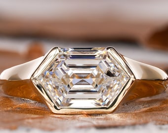May include: A gold engagement ring with a hexagonal setting featuring a large, clear, emerald-cut diamond.