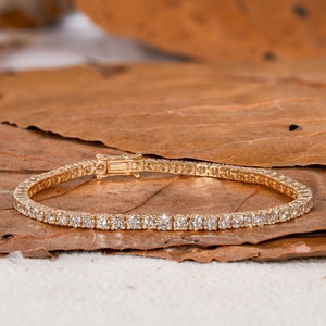 Puede incluir: Un brazalete de tenis de oro con una fila de pequeños diamantes transparentes.