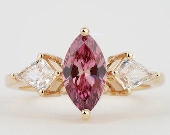 Puede incluir: Un anillo de oro con una piedra preciosa rosa en forma de marquesa y dos piedras triangulares más pequeñas y transparentes a cada lado.