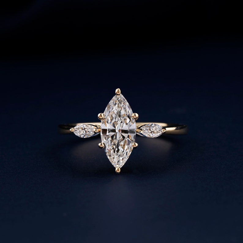 Pu&ograve; includere: Un anello d'oro con un grande diamante a forma di marquise al centro e due diamanti pi&ugrave; piccoli a forma di pera su entrambi i lati.