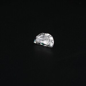May include: A clear, faceted, half-moon shaped diamond gemstone on a black background.