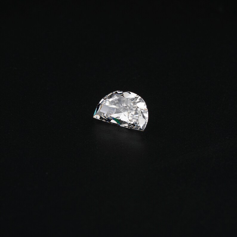 May include: A clear, faceted, half-moon shaped diamond gemstone on a black background.