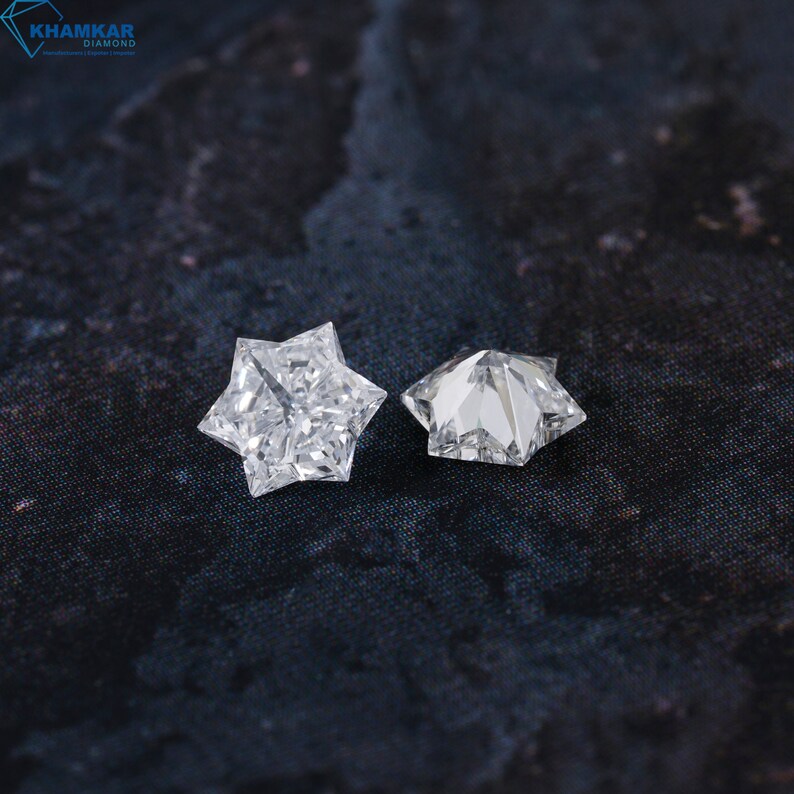 May include: Two clear star-shaped diamonds on a dark gray textured surface.