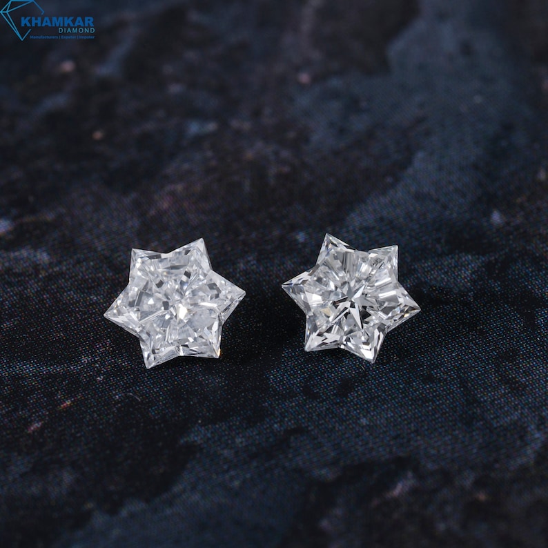 May include: Two clear star-shaped diamonds on a dark gray textured surface.