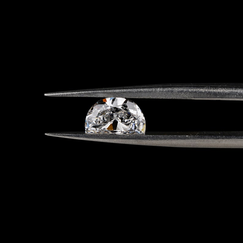 May include: A clear, round diamond gemstone held in silver tweezers against a black background.