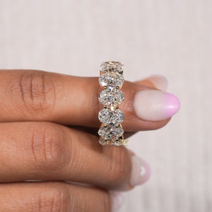May include: A gold band ring with a row of oval-shaped diamonds set in a halo style.