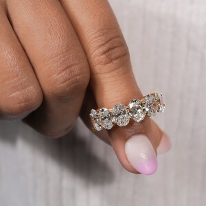 May include: A gold band ring with a row of oval-shaped diamonds. The ring is set in a pave setting.