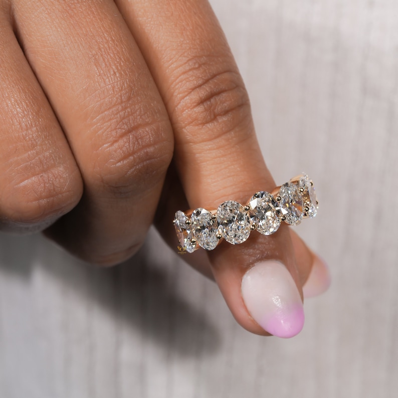 May include: A gold band ring with a row of oval-shaped diamonds. The ring is set in a pave setting.
