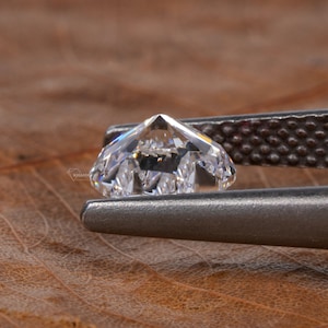 Op de afbeelding: Een heldere, gefacetteerde diamant vastgehouden in een metalen pincet. De diamant is briljant geslepen en heeft een hoge mate van glans.