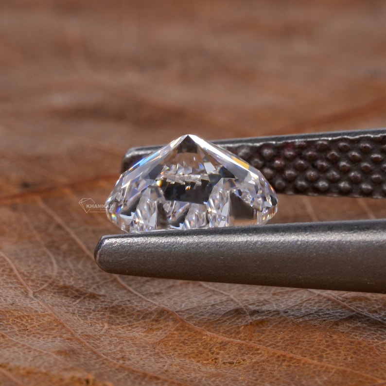 Op de afbeelding: Een heldere, gefacetteerde diamant vastgehouden in een metalen pincet. De diamant is briljant geslepen en heeft een hoge mate van glans.