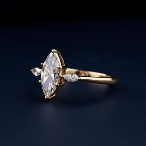 Pu&ograve; includere: Un anello di fidanzamento in oro con un grande diamante a forma di marquise e due diamanti pi&ugrave; piccoli a forma di pera sulla fascia.
