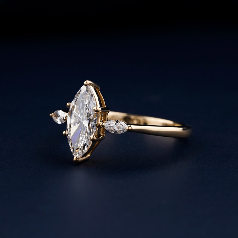 Pu&ograve; includere: Un anello di fidanzamento in oro con un grande diamante a forma di marquise e due diamanti pi&ugrave; piccoli a forma di pera sulla fascia.