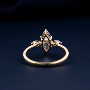 Pu&ograve; includere: Un anello d'oro con una pietra centrale a forma di marquise e due diamanti pi&ugrave; piccoli su entrambi i lati. L'anello &egrave; posto su uno sfondo blu scuro.