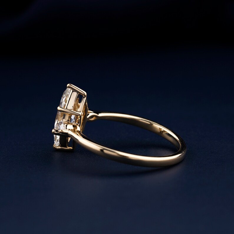 Pu&ograve; includere: Un anello d'oro con un grande diamante chiaro a forma di marquise incastonato a griffe. L'anello &egrave; su uno sfondo blu scuro.
