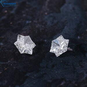 May include: Two clear, faceted, star-shaped diamonds on a black background.