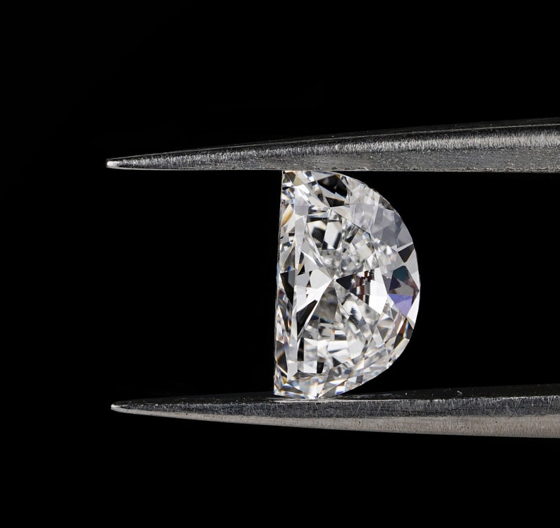 May include: A clear, faceted diamond gemstone held in a pair of silver tweezers against a black background.