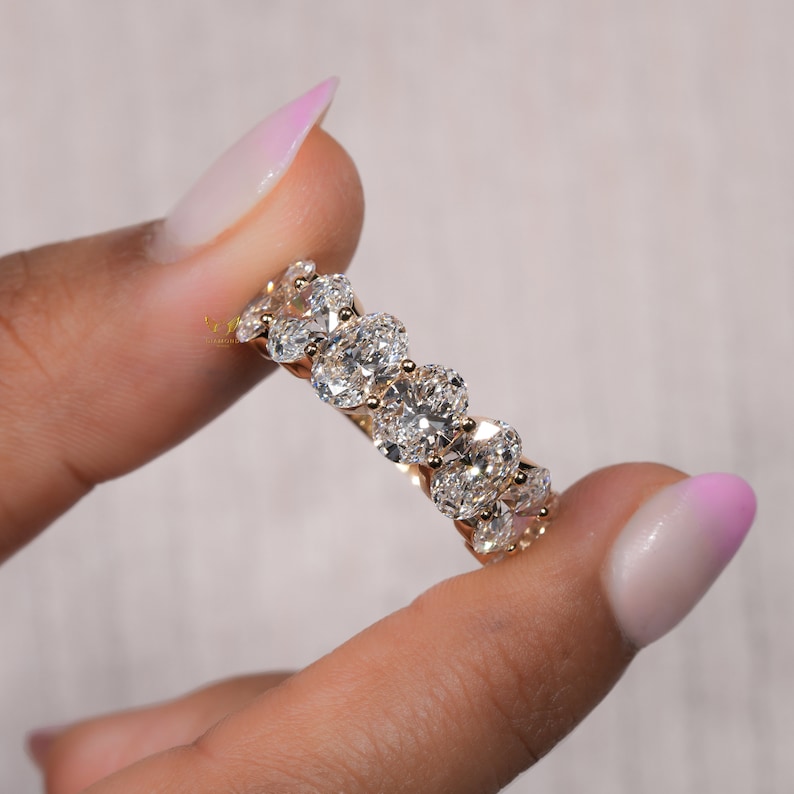 May include: A gold band ring with a row of oval-shaped diamonds set in a pave setting.