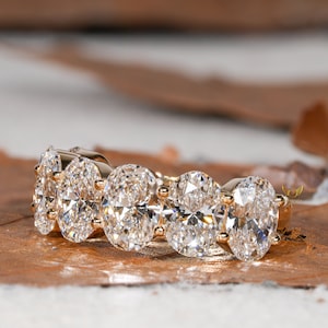 May include: A gold band ring with five oval-shaped diamonds set in a row. The diamonds are clear and sparkly.