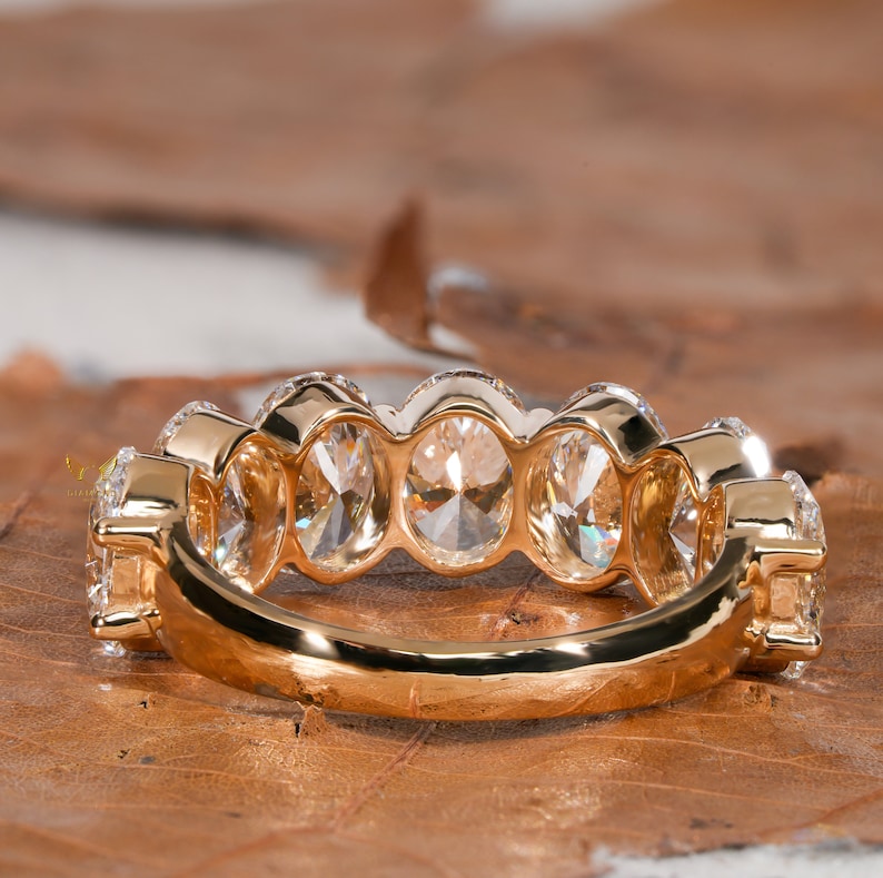 May include: A gold band ring with a row of oval-shaped diamonds set in a pave setting.