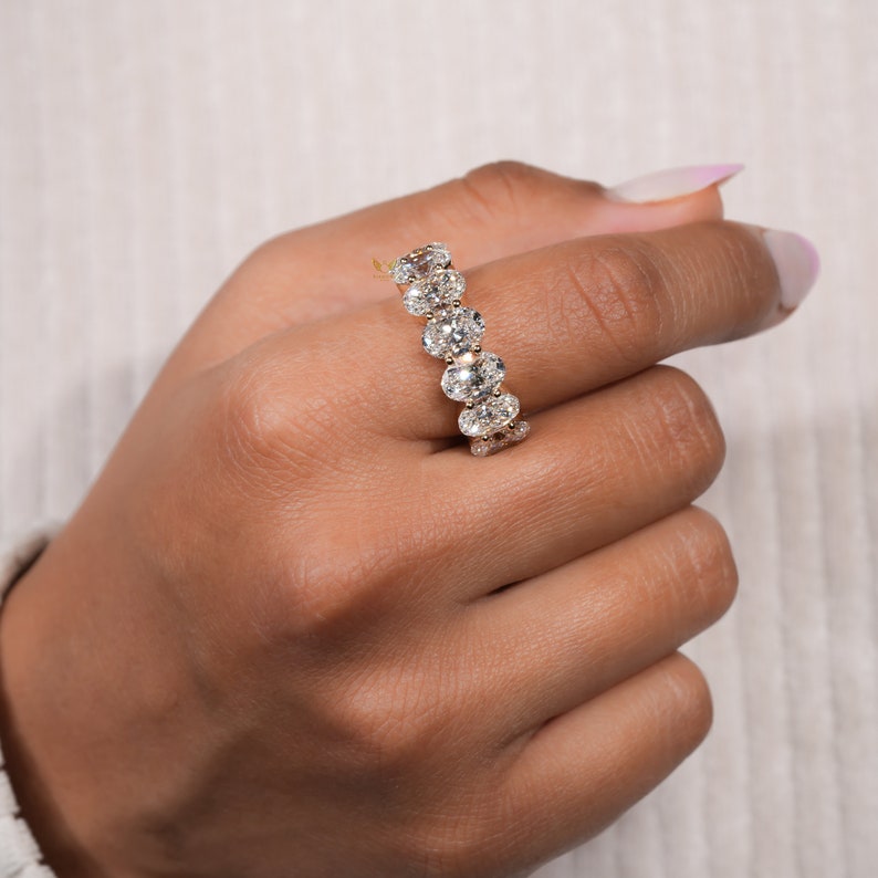 May include: A gold band ring with a row of oval-shaped diamonds set in a pave setting.