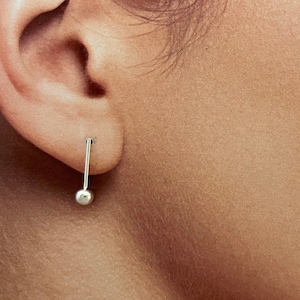 May include: A silver stud earring with a small ball at the end. The earring is worn in the left ear.